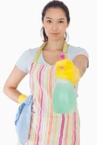Smiling woman spraying cleaner in apron and rubber gloves